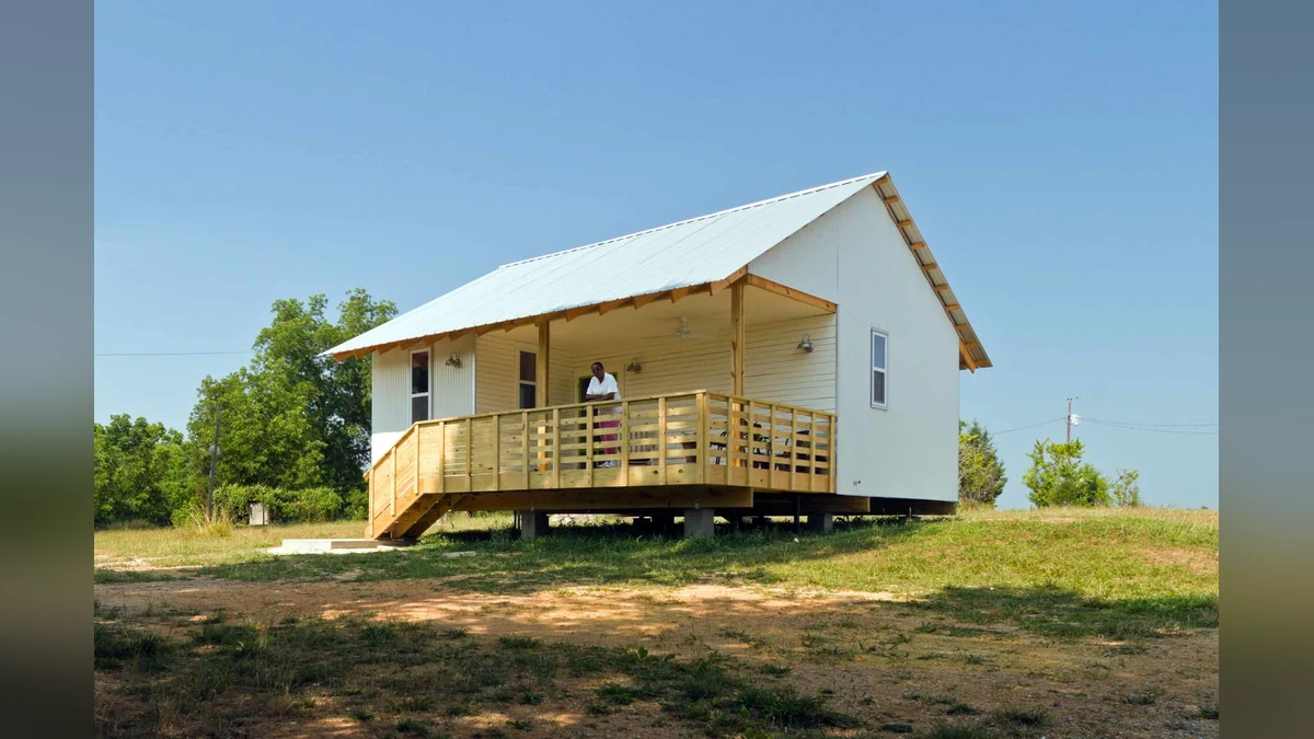 A completed Rural Studio house with a small graphic changing the $20K build target to total cost of ownership.